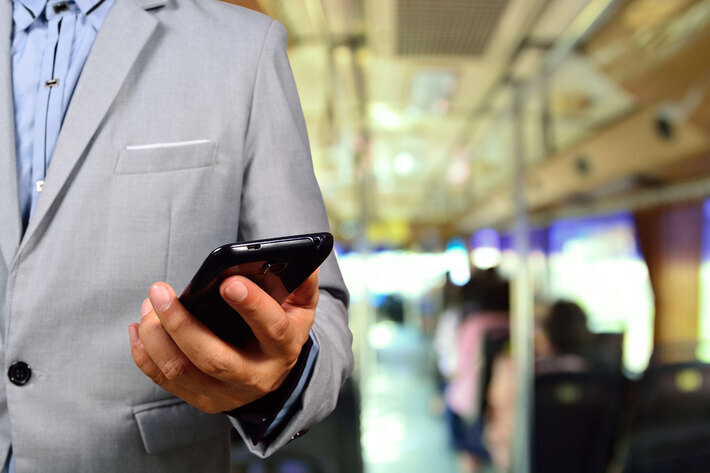 Eine Person mit Anzug hat ein Handy in der HAnd. 