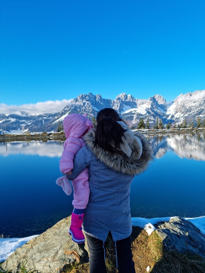 Man sieht Lisa mit der Tochter auf dem Arm von hinten, die auf eine Schneelandschaft schauen.