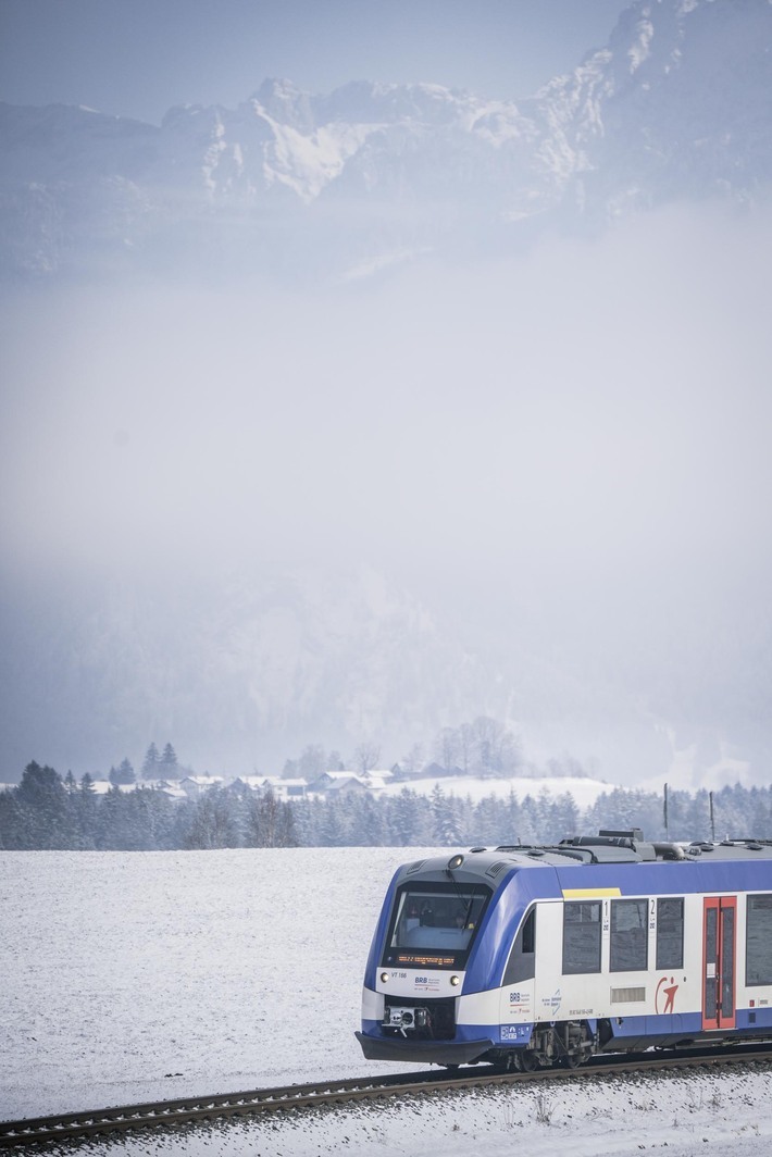 Ein LINT-Zug der BRB fährt am Hopfensee mit Bergen im Hintergrund. 