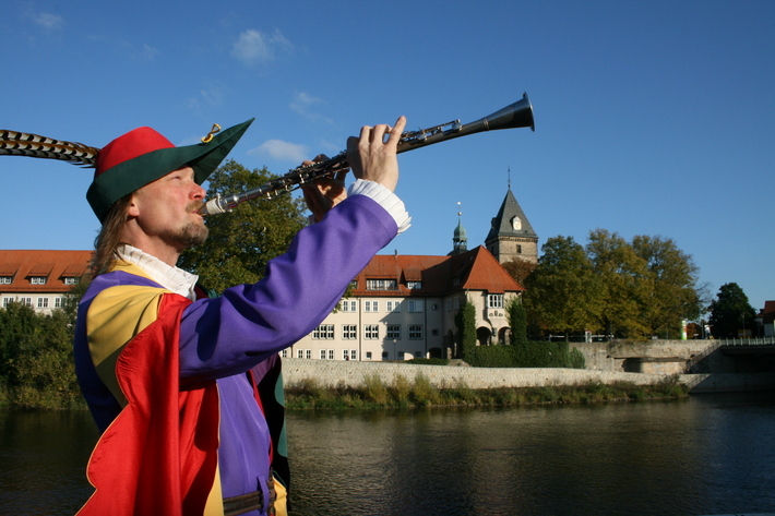 Der Rattenfänger spielt eine Flöte. Weser im Hintergrund.
