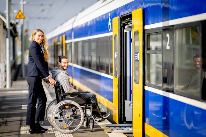 Mitarbeiterin hilft Mann im Rollstuhl in den Zug
