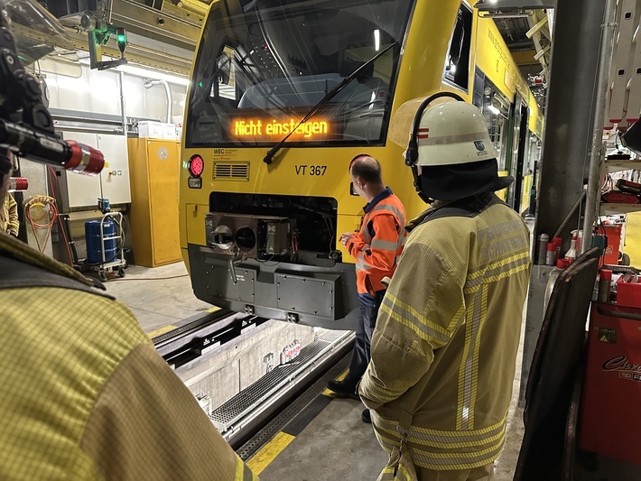 Feuerwehrleute stehen um ein Fahrzeug des Typs RegioShuttle der Strohgäubahn in einer Werkstatthalle. Vor dem Fahrzeug steht ein Mitarbeiter der WEG